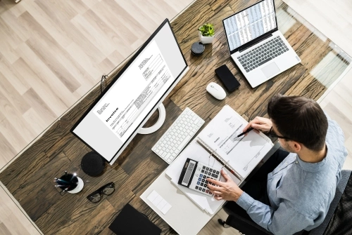 A CPA works on a computer and uses a calculator to file a tax extension for a client.