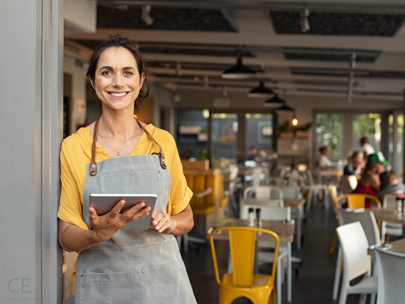 Female restaurant owner smiling with iPad. This image complement the blog addressing "married couple sole proprietorship or partnership" and "can a married couple file as a qualified joint venture?"