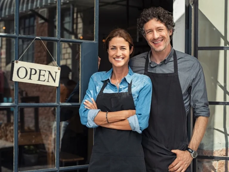 Two business owners smiling in front of the entrance. This image complements the blog addressing married couple sole proprietorship or partnership.