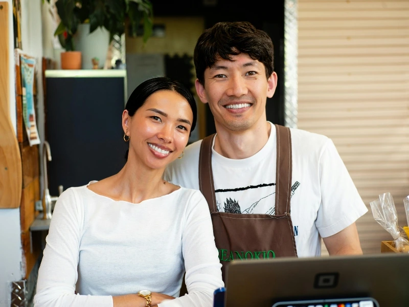 Couple cafe owners smiling behind the counter. This image complements the blog addressing married couple sole proprietorship or partnership.