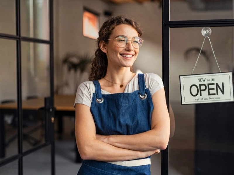 Female cafe owner smiling at entrance. This image complements the blog addressing married couple sole proprietorship or partnership.