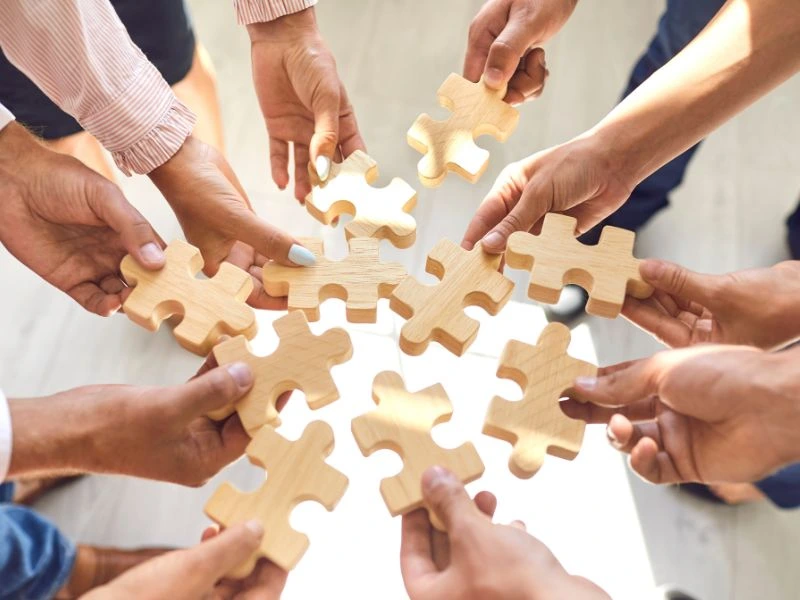 Hands holding puzzle pieces in a circle to showcase What is a Statutory Employee vs Traditional Employee