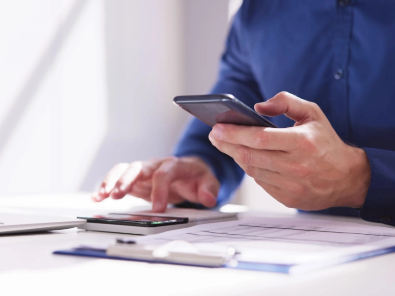Masculine hand uses a phone and calculator to file taxes. Image accompanies the blog "Common Tax Mistakes." 