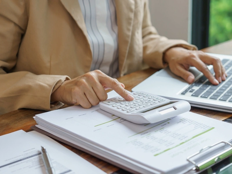 Woman typing on calculator, exploring the pros and cons of filing a tax extension.