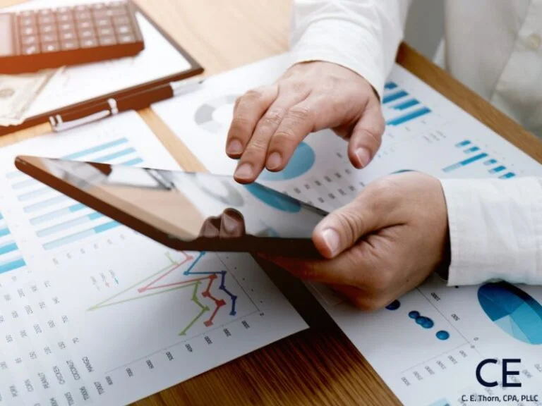 A Raleigh CPA is calculating service revenue by using a calculator and looking at pie charts and line graphs.